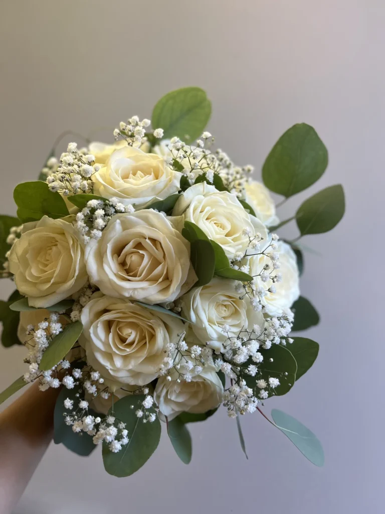 En bukett med vita rosor, blåsippor och eukalyptusblad hålls mot en ljus bakgrund.