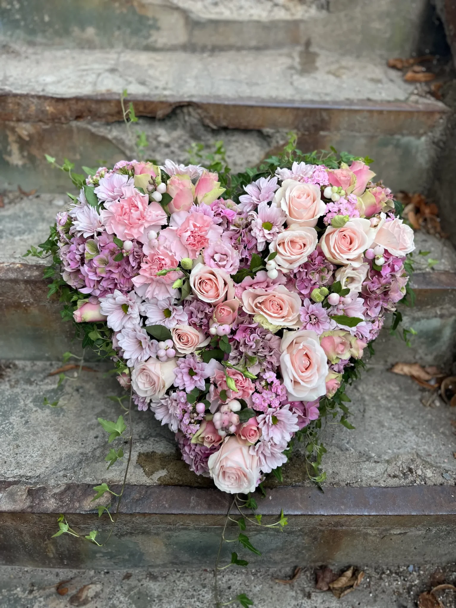 Ett hjärtformat blomsterarrangemang med rosa och vita blommor är placerat på väderbitna betongtrappor.