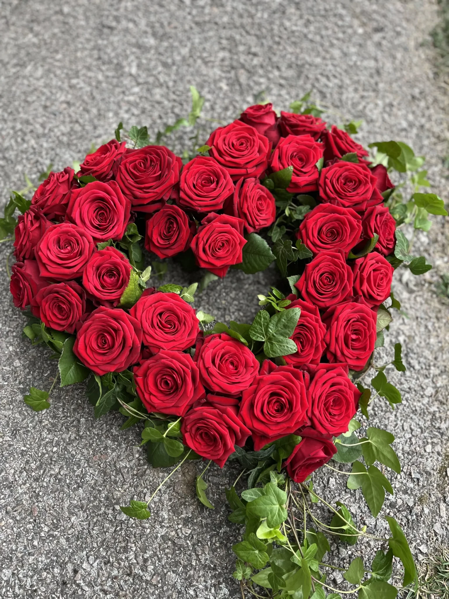 Ett hjärtformat arrangemang av röda rosor med gröna bladaccenter placerade på en grov stenyta.